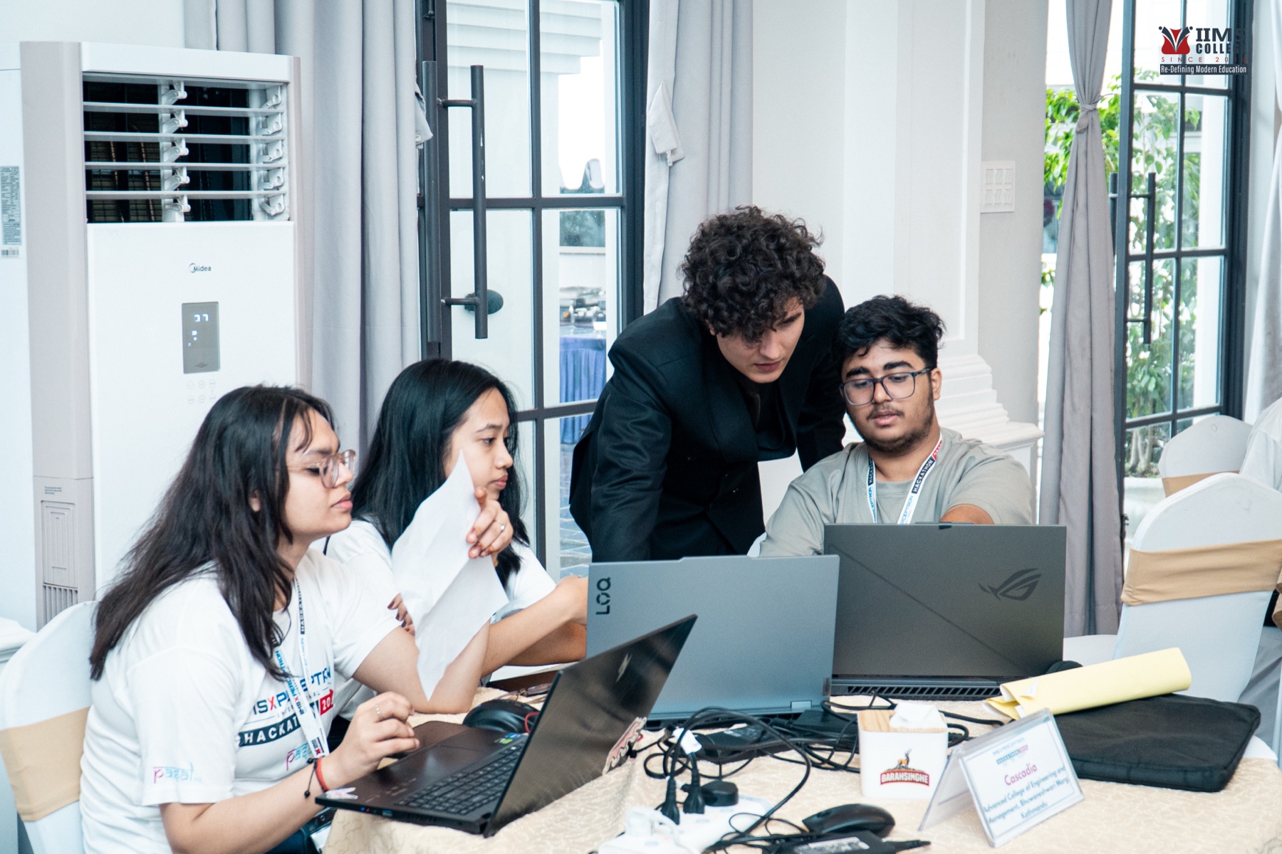 A mentor leaning over several laptops while working directly with a participant team